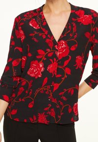 Blusa nera con bottoni, caratterizzata da stampa floreale rossa, scollo a V e maniche a tre quarti con risvolto. Tessuto morbido e leggero.