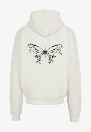 Hvit hettegenser med grafikk av en svart sommerfugl på baksiden, kombinert med mørke denimbukser og svarte sko, med ribbestrikkede mansjetter og nederkant.