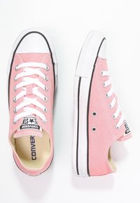 Niskie różowe trampki z płótna z białymi gumowymi podeszwami, sznurówkami i czarnymi detalami w paski, zaprezentowane w widokach z góry i z boku.