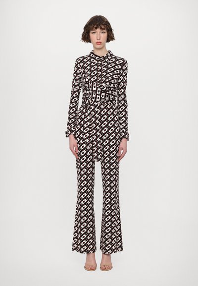 Langärmliger Jumpsuit im schwarz-weißen geometrischen Muster. Verfügt über einen Kragen, einen gefältelten Vorderteil, eine taillierte Taille und weite Hosenbeine.