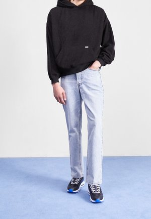 Zwarte hoodie met structuur en een kangoeroezak, gecombineerd met lichtblauwe jeans met rechte pijpen en zwarte sneakers met blauwe accenten.