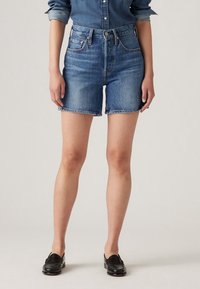 Shorts de mezclilla en azul claro con cintura alta, dobladillo deshilachado y diseño de cinco bolsillos. Combinados con mocasines negros planos sin calcetines.
