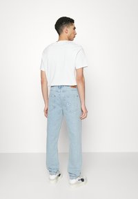 Jeans de color azul claro con un corte relajado, que cuentan con bolsillos traseros y un sutil detalle bordado en blanco. Combinados con una camiseta blanca básica y zapatillas.