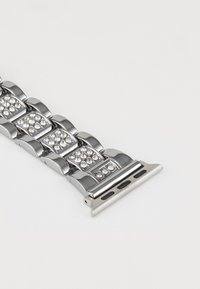 Bracelet de montre en métal présentant une finition argentée polie, incrusté de strass clairs, avec un fermoir argenté mat contrastant.
