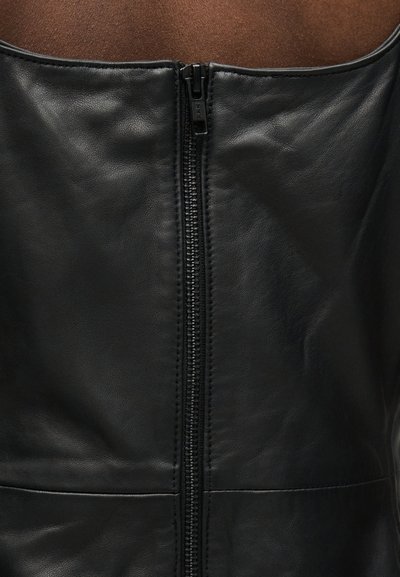 Μαύρο δερμάτινο ένδυμα με μαύρο φερμουάρ στο κέντρο, που δείχνει υφή υλικού και λεπτομέρειες ραφής στην άνω περιοχή του κορμού.