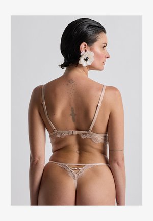 Completo di lingerie beige rifinito in pizzo con spalline regolabili, caratterizzato da motivi delicati e chiusura a gancio sul retro.