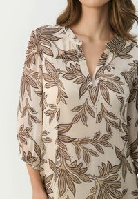 Beige Bluse mit V-Ausschnitt, die komplizierte braune Blattmuster und Dreiviertelärmel aufweist. Glattes, leichtes Gewebe mit einer zarten Textur.