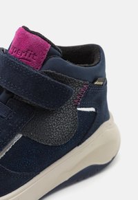 Dětská kotníková obuv v námořnické modři s suchým zipem, texturovanými prvky a světlou podešví s posypem.