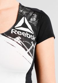 Svart och vit sporttop med Reebok-logotyp, korta ärmar, rund halsringning och en strukturerad grafisk mönstring.