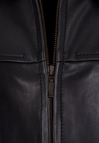 Vue en gros plan d'une veste en cuir noire partiellement dézippée avec des coutures visibles et une fermeture éclair métallique couleur bronze.