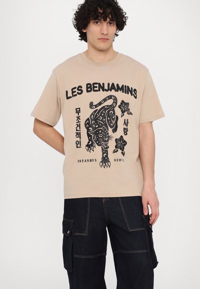 T-shirt en coton beige avec un graphisme noir d'un léopard et de fleurs, accompagné du texte "LES BENJAMINS ISTANBUL SEOUL." Manches courtes.