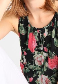 Haut noir avec un motif floral de roses roses et de feuilles vertes, en tissu léger, avec un design plissé au niveau de l'encolure.