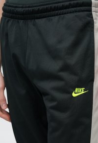 Μαύρο αθλητικό παντελόνι από απαλό πολυεστέρα, με πράσινο λογότυπο Nike και ανοιχτό γκρι πλαϊνή φάσα, με ελαστική μέση.