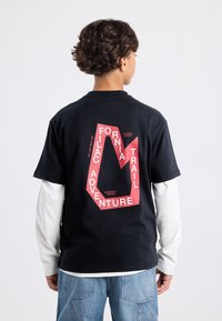 Musta puuvillapaita, jossa on suuri punainen graafinen kuvio, jossa lukee "CALIFORNIA TRAIL ADVENTURE" geometrisessa asetelmassa.