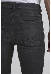 Black denim jeans with a sleek finish, featuring a standard back pocket design and subtle stitching details. Material appears sturdy and textured.