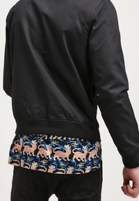 Chaqueta bomber negra con una textura suave, que presenta un forro colorido y estampado de tigres y acentos azules a lo largo del dobladillo.