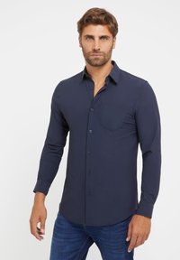 Majica dugih rukava tamnoplavih boja s ovratnikom na dugme, jednim džepom na prsima i glatkom teksturom. Ima gumbe sprijeda i slim fit dizajn.