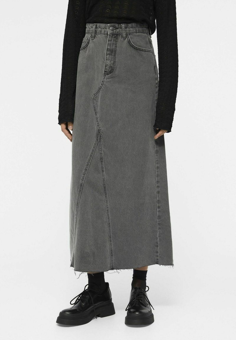 Jupe longue en denim gris taille haute avec coutures asymétriques portée avec des chaussures à plateforme noires à lacets et un haut noir à manches longues.