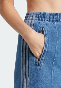 Joggers de denim con cintura elástica, bolsillos laterales con cremallera y costuras de acento en gris. La tela tiene un acabado suave y texturizado.