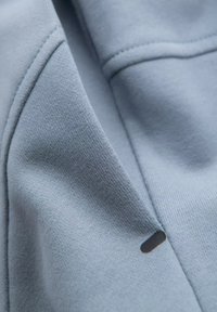 Tissu bleu clair avec une texture lisse, des détails de couture subtils et une petite étiquette noire. Le matériau semble doux et flexible.