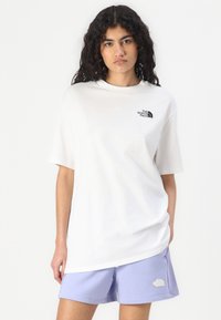 Lightweight white cotton t-shirt with a round neck and short sleeves, featuring a black logo on the left chest. Paired with lavender shorts.