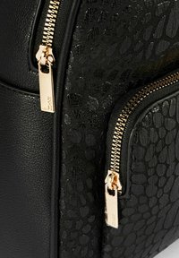 Czarny plecak z teksturowanej skóry, z złotymi zamkami błyskawicznymi, dwoma zamykanymi na zamek przegrodami i subtelnym tłoczonym wzorem.