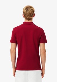 Bordeauxkleurig poloshirt van katoen, met een klassieke kraag en korte mouwen, gladde textuur, met een eenvoudig ontwerp en zonder zichtbaar logo.