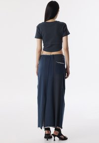 Granatowy crop top z krótkimi rękawami w połączeniu z długą granatową spódnicą z bocznym rozcięciem i tylną kieszenią, wykończoną postrzępionymi krawędziami.