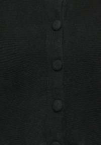 Sort tekstureret cardigan med runde stofknapper langs midten foran, der fremhæver et ribbet mønster og blødt materiale.