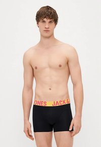 Zwarte boxershorts met een gele tailleband waarop 'JACK & JONES' in roze letters staat. Gladde stof en een strakke pasvorm. Model is zonder shirt.
