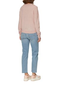 Lichtroze gebreide trui met een ontspannen pasvorm, gecombineerd met lichtblauwe rechttoe-rechtaan jeans en stevige witte en roze sneakers.