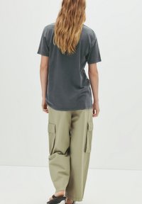 T-shirt oversize gris charbon à manches courtes, associé à un pantalon cargo large vert olive clair avec de grandes poches latérales.