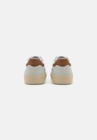 Zapatillas con parte superior de cuero blanco, detalles en gamuza gris y parche de cuero marrón en el talón. Punta redondeada y suela de goma beige.