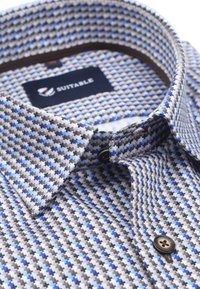 Blauw en grijs gestreept shirt met een button-down kraag, bruine knoopaccenten en een stoffen label met het logo "SUITABLE".