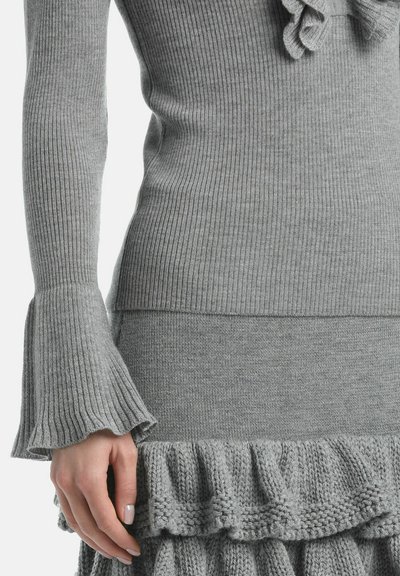 Gray knit sweater features ribbed texture and bell sleeves. The lower section has a ruffled hem, complementing the fitted silhouette.