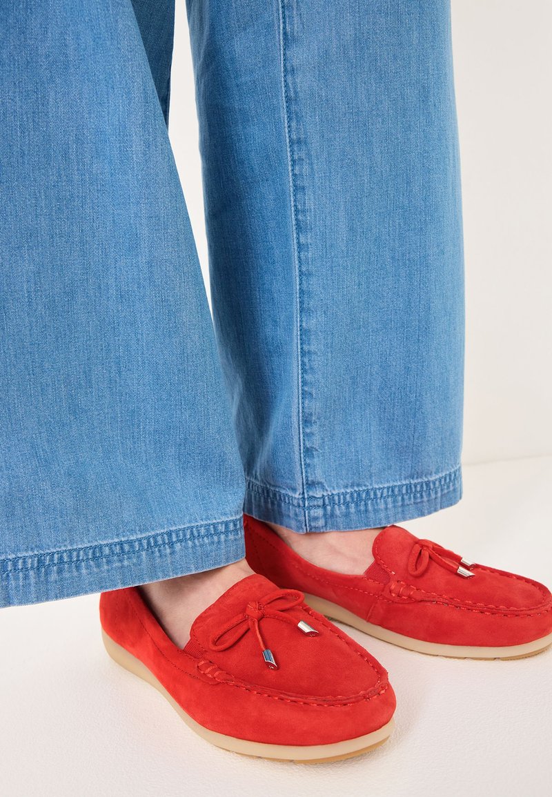 Rode suède moccasinstijl schoenen met een ronde neus, veters en zilveren accenten, gecombineerd met lichtblauwe wijde jeans.