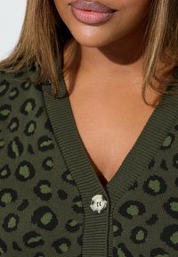 Olivgrüner Cardigan mit schwarzem Leopardenmuster, mit V-Ausschnitt und einem runden Knopfverschluss, aus strukturiertem Strickmaterial gefertigt.