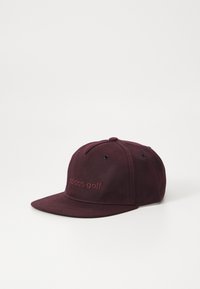 Burgunderfarget baseball-caps med brodert "adidas golf"-logo, flat skjerm, seks paneler og ventilasjonsøyne. Laget av slitesterkt stoff.