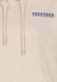 Lichtbeige hoodie met witte koorden, met daarop in donkerblauw gedrukt: "SAMEN ZIJN DIT MIJN SOORT MENSEN." Gladde stoftextuur.