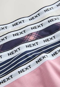 Primer plano de bandas de tela con el texto repetido "NEXT", mostrando patrones que incluyen rosa liso, cuadros azul marino y rayas azul marino debajo de las bandas blancas.