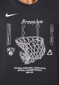 Camiseta de algodón negra con gráficos blancos de un aro de baloncesto, "Brooklyn NETS" y la marca oficial de Nike abajo.