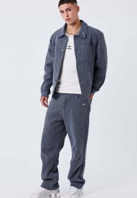 Ensemble veste et pantalon à carreaux bleu marine en tissu texturé, avec poches avant et chemise à col rond en dessous. Baskets blanches.