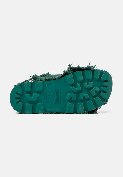 Grön skosula med texturerad gummi och djupa mönster. Ovandelen har fransade kanter, med "Camper"-logotyp synlig på mellansulan.
