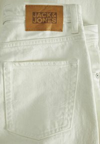 Bijele traperice s leđnim džepom i smešnim kožnim komadom s utisnutim natpisom "JACK & JONES". Glatka tekstura i klasičan dizajn.