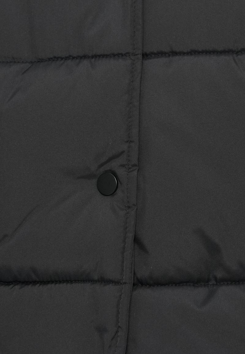 Gros plan sur une doudoune noire, présentant des sections matelassées, une texture lisse et mate, ainsi qu'un détail de bouton-pression noir rond.