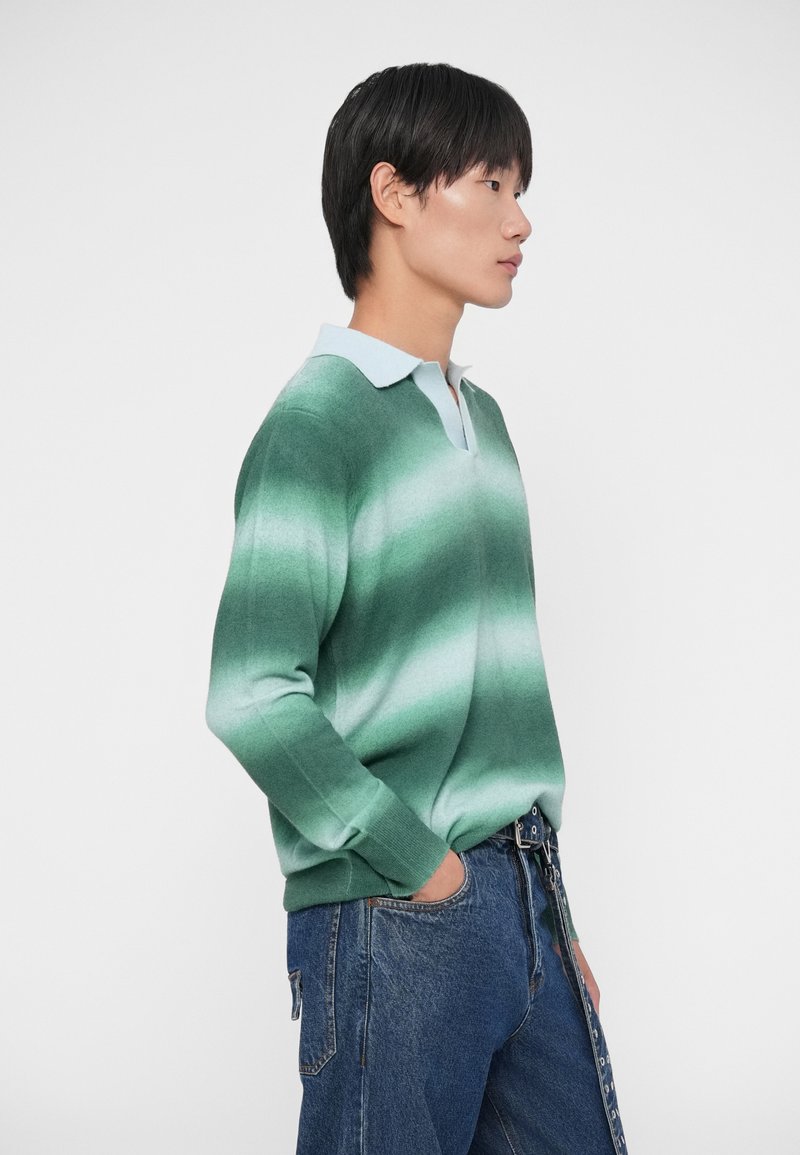 Green gradient sweater with a light blue collar, made of soft material. Features a V-neck and long sleeves; worn with loose denim jeans.