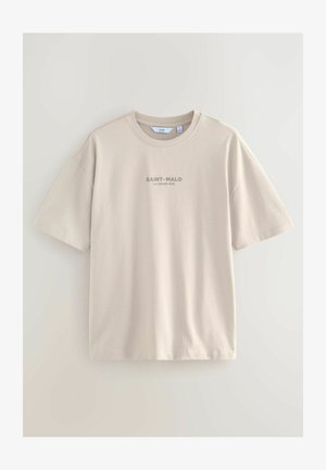 T-shirt beige a maniche corte realizzato in tessuto morbido; presenta un collo tondo e la scritta "SAINT-MALO LA GRAND RUE" stampata in grigio scuro sul davanti.