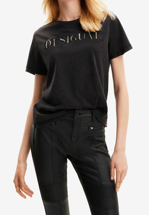 Zwarte katoenen t-shirt met geborduurd logo, gecombineerd met zwarte leren broek met ritszakken en geribbelde textuur op de knieën.