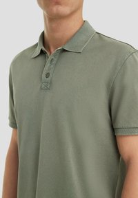Groene katoenen polo-shirt met een kraag, een twee-knopen-sluitsysteem en korte mouwen. Kenmerkt zich door een textuurstof en een kleine driehoekige stikdetail.