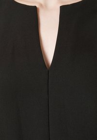 Black garment with a V-neckline and minimalistic design. The fabric appears smooth with a matte finish. Center seam runs down the front.